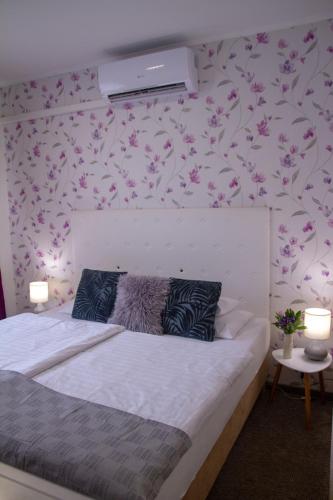 1 dormitorio con cama blanca y papel pintado de flores rosas en Amfora Panzió, en Gyula