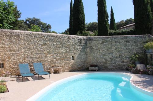 une piscine avec deux chaises et un mur en pierre dans l'établissement Le Mazet, gîte des Lucioles en Provence, à Montségur-sur-Lauzon