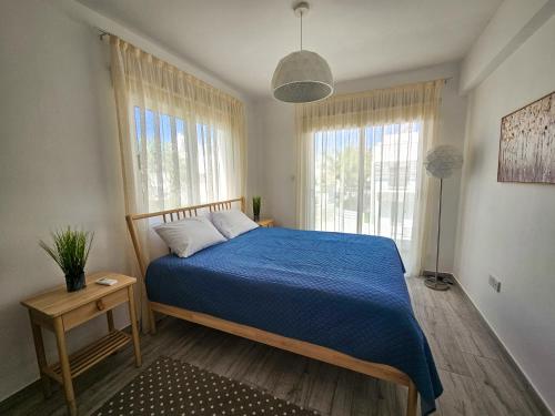 a bedroom with a bed with a blue comforter and two windows at Nissi beach villa Azure in Ayia Napa