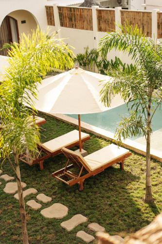 an umbrella and two chaise lounges next to the ocean at TWINFIN Surf House in Kuta Lombok