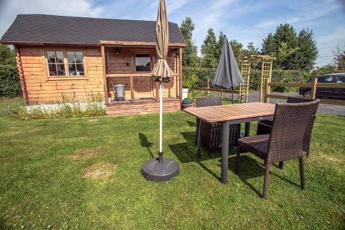 a table and an umbrella in a yard with a cabin at Wooden Lodge in Saint-Blimont