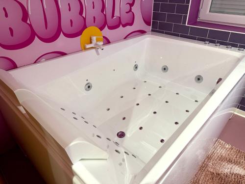 a bathtub in a bathroom with a pink tiled wall at Capsule Bubble Jacuzzi Sauna Switch 2 in Maubeuge