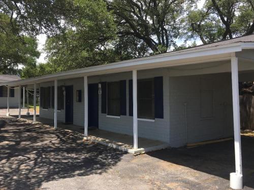 a white house with a porch with trees in the background at La Vista Motel in Burnet