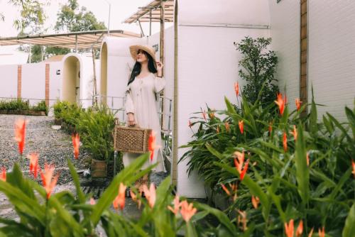 a woman in a white dress and hat standing next to a garden at ภูสกาย โฮมสเตย์ in Mon Jam