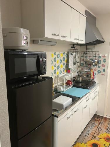 a kitchen with a black refrigerator and white cabinets at MINPAKUx櫻花 in Osaka