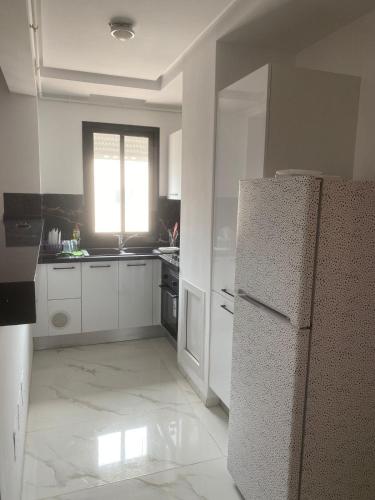 cocina blanca con nevera y ventana en Apart s2 ain zaghouen la marsa, en La Marsa