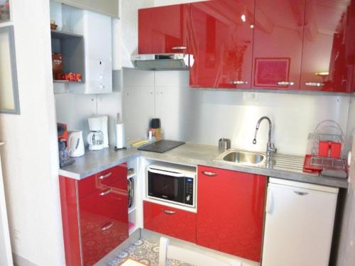 une petite cuisine avec des armoires rouges et un évier dans l'établissement Appartement climatisé pour 5 pers avec terrasse, à 900m de la plage et parking privatif - FR-1-607-66, au Cap d'Agde