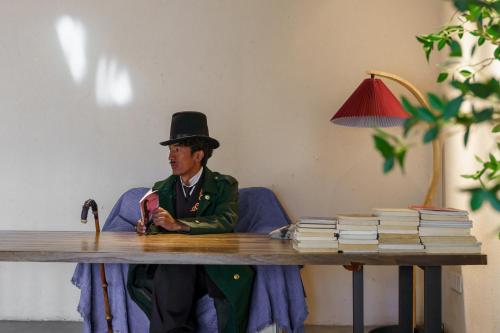 a man in a top hat sitting at a table with books at 沙溪坡上村花隐世民宿 in Diannan