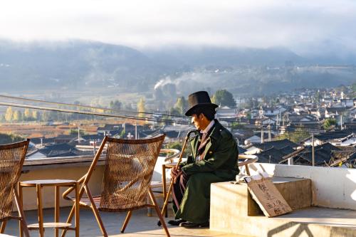 a man in a top hat sitting on a ledge at 沙溪坡上村花隐世民宿 in Diannan