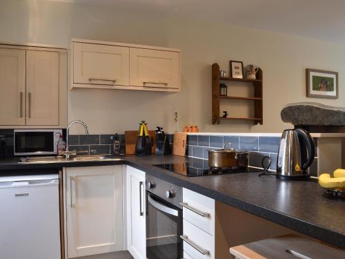 a kitchen with white cabinets and black counter tops at Coopers Cottage in Haverthwaite