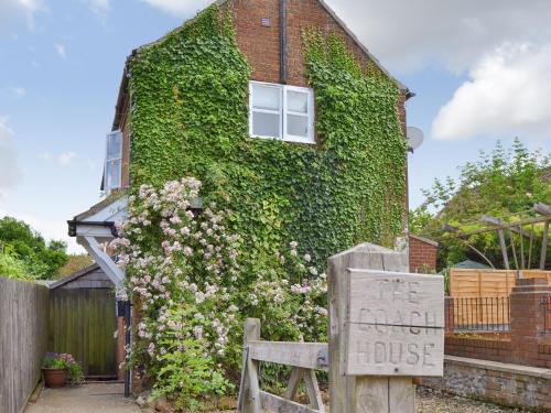 a ivy covered house with a sign in front of it at The Coach House in Great Ryburgh