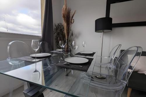 une table à manger en verre avec des chaises et des verres à vin dans l'établissement 3 pièces lumineux, balcon & parking - Paris 20 min, à Sartrouville