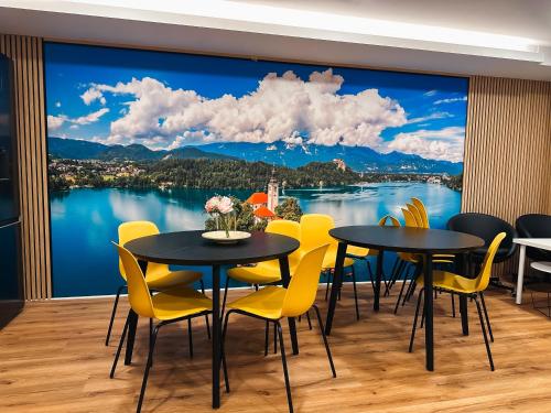 a room with two tables and yellow chairs and a large window at Central Hostel Lesce-Bled in Lesce