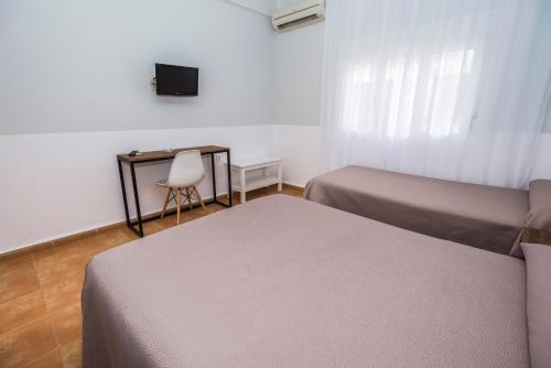 two beds in a room with a chair and a television at Hostal Las Cumbres in Conil de la Frontera