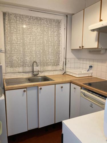 une cuisine avec des armoires blanches, un évier et une fenêtre dans l'établissement Beau 2P à Deauville avec balcon, à La Celle-sous-Gouzon