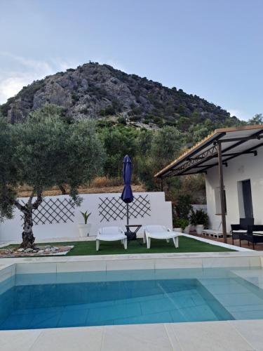 a pool with two chairs and a blue umbrella at Casa Puerto Blanco II in Algodonales