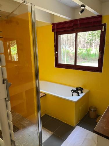 une salle de bains jaune avec baignoire et fenêtre. dans l'établissement La Balinaise, à Hourtin