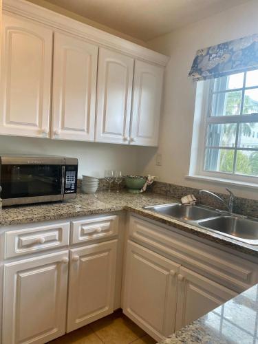 a kitchen with white cabinets and a sink and a microwave at NEW Oceanfront Condo in George Town in George Town