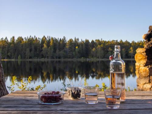 a bottle of alcohol and two glasses on a table near a lake at Holiday Home Myckla by Interhome in Hudiksvall