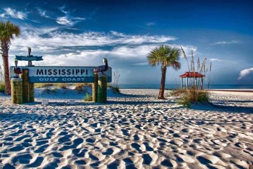 a sign on a beach with palm trees and the ocean at Cheerful 3 bedroom townhome Pool! Beach! Fun! in Gulfport