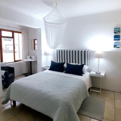 a white bedroom with a large bed with blue pillows at Mclaren Self Catering in Gansbaai
