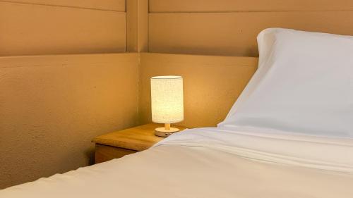 a bed with a white pillow and a lamp on a table at Kampung Nature Stilt House with Paddy Field View in Balik Pulau