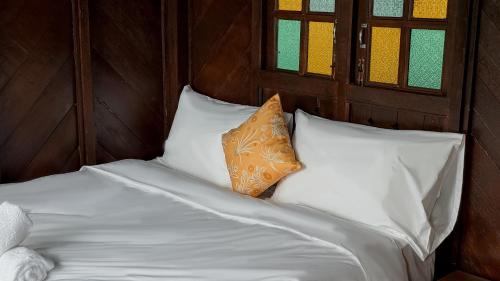 a bed with white sheets and an orange pillow at Kampung Nature Stilt House with Paddy Field View in Balik Pulau