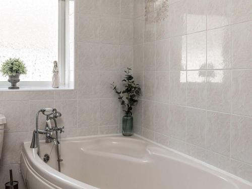 baño con bañera blanca y jarrón de flores en The Crows Nest, en Buxton