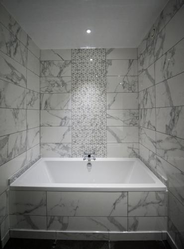 a white bath tub in a bathroom with marble tiles at Parklands Hotel & Country Club in Newton Mearns