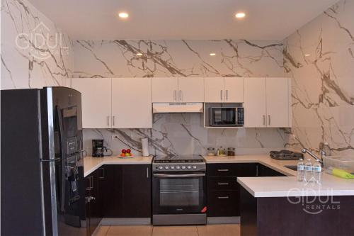 Una cocina con refrigerador negro y gabinetes blancos. en Volcano Views Apartment, en San Salvador