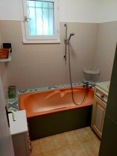 La salle de bains est pourvue d'une baignoire orange et d'une fenêtre. dans l'établissement Bas de villa, terrasse au calme, à Gattières
