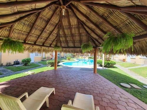 a patio with a straw umbrella and chairs and a pool at Casa de 3 habitaciones con alberca in Ixtapa
