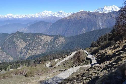 a winding road on a mountain with snow covered mountains at Ejaa's House Bistro & Cafe in Rishīkesh