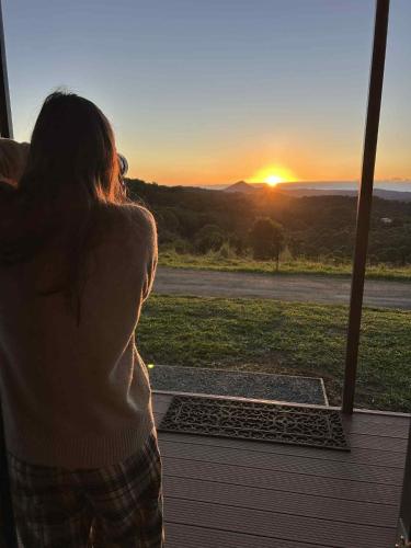 a woman looking out a window at the sunset at Narnoomia Farm Cottage in Belli Park
