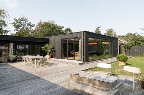 a black house with a deck with a table and chairs at Modern Exclusivity In 60S House Near Dyngby Beach in Odder