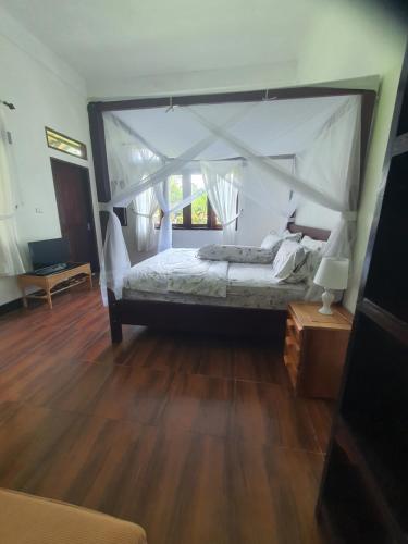 a bedroom with a canopy bed with a wooden floor at Sumatra Cheeky Monkeys Villa, Trekking and Tours in Bukit Lawang