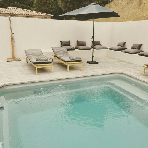 une piscine avec deux chaises longues et un parasol dans l'établissement Stone Sheepfold With Sea View In Corsica, à Sari-dʼOrcino