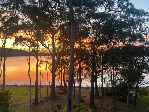 a sunset over a body of water with trees at The Lake House on Amaroo in Smiths Lake