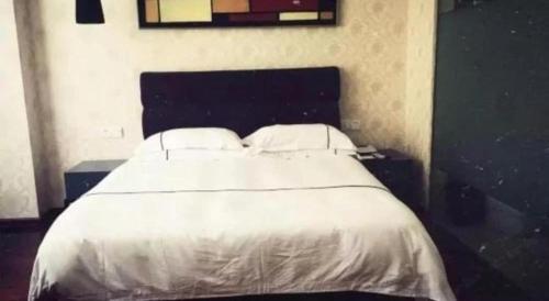 a white bed with two pillows in a bedroom at Yiwu Baiheng Hotel in Yiwu