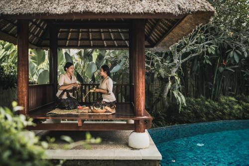 two women sitting on a bench next to a swimming pool at The Retreat at Kharista by Ekosistem in Canggu