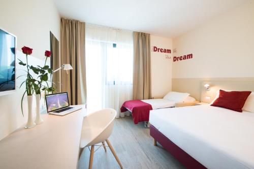 a hotel room with two beds and a desk with a laptop at Airport Hotel Bergamo in Bagnatica