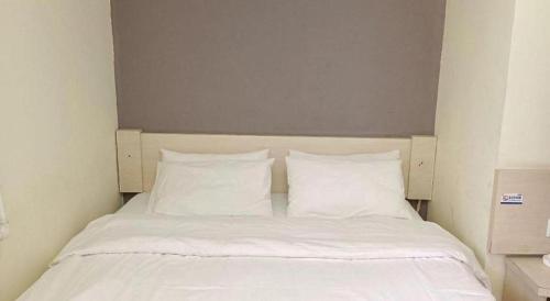 a bed with white sheets and pillows in a room at 7 Days Inn Hami Baofeng Market in Qumul