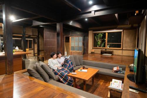 two people sitting on a couch in a living room at 五島列島おぢか島 古民家ステイ Ojika Island Kominka Stay in Ojika