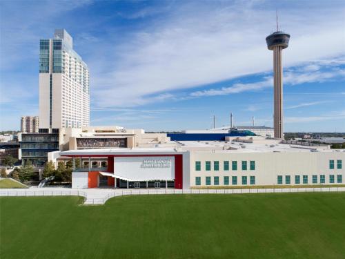 a building with a green field in front of a city at Grand Hyatt San Antonio River Walk in San Antonio