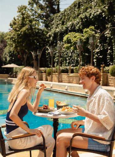 a man and woman sitting at a table eating food by a pool at Grand Hyatt Istanbul in Istanbul