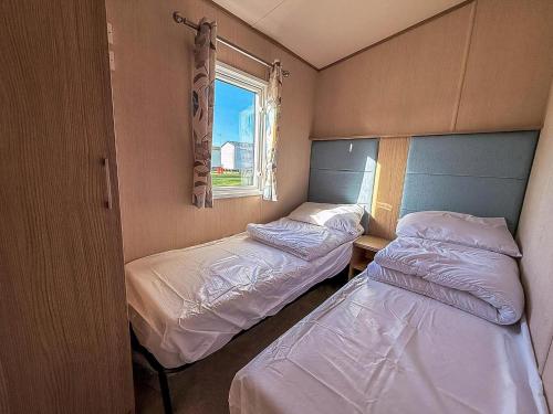 two beds in a small room with a window at Fantastic Caravan With Decking At Haven Hopton Holiday Park Ref 80069G in Great Yarmouth