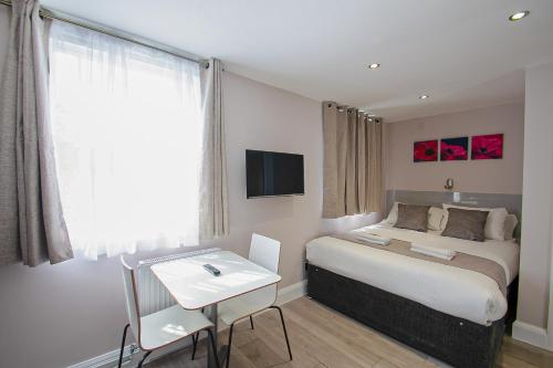 a bedroom with a bed and a table and a tv at Imperial Court Studios in London