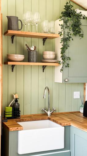 a kitchen with a sink and shelves with dishes at Cnocvann Croft Shepherd Huts in Kilmorack