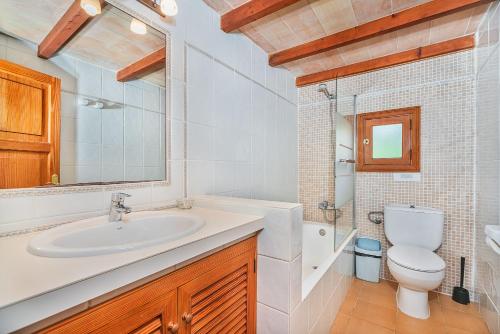 Un baño con lavabo, inodoro y espejo. en Tintorer, en Puerto Pollensa