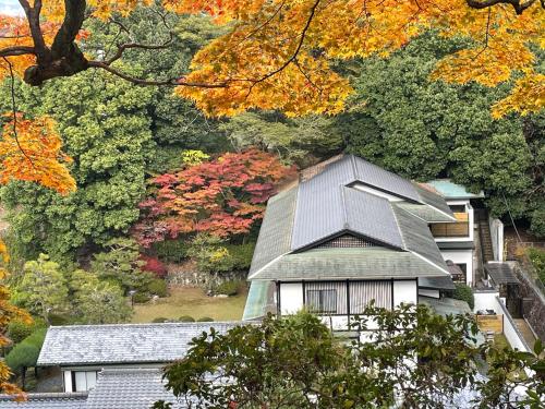 a house with a pitched roof in front of trees at Miyajima Guest House Mikuniya in Miyajima